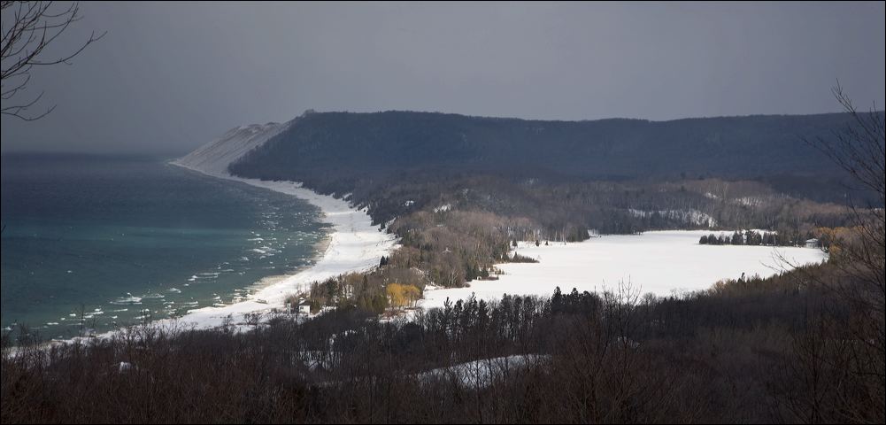 A winter snow squall approaches the Sleeping Bear Dunes while sun highlights North Bar Lake and the Empire Beach, as viewed from the lookout on the Bluffs trail.